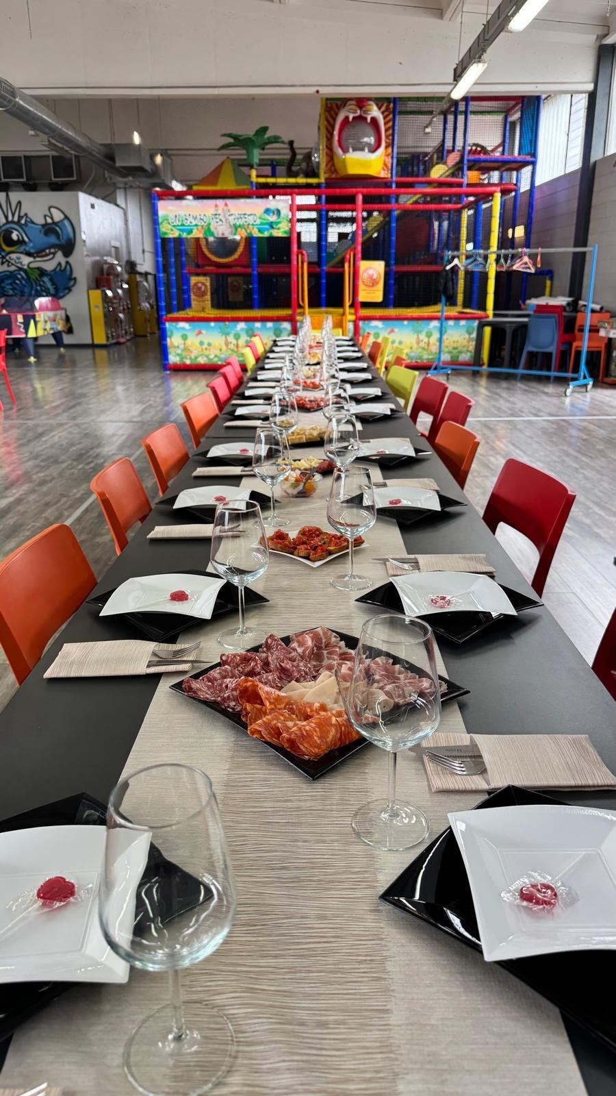 Sala eventi di Pito Pitù apparecchiata per una cerimonia, con il parco giochi al coperto sullo sfondo